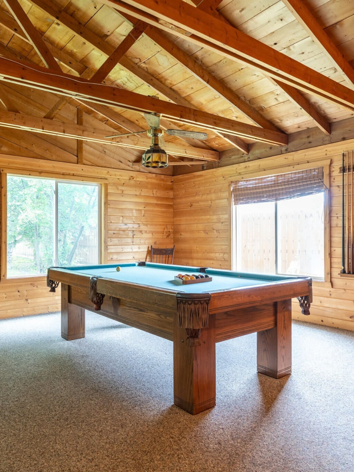 Wood-paneled game room with a pool table under a vaulted ceiling with exposed beams