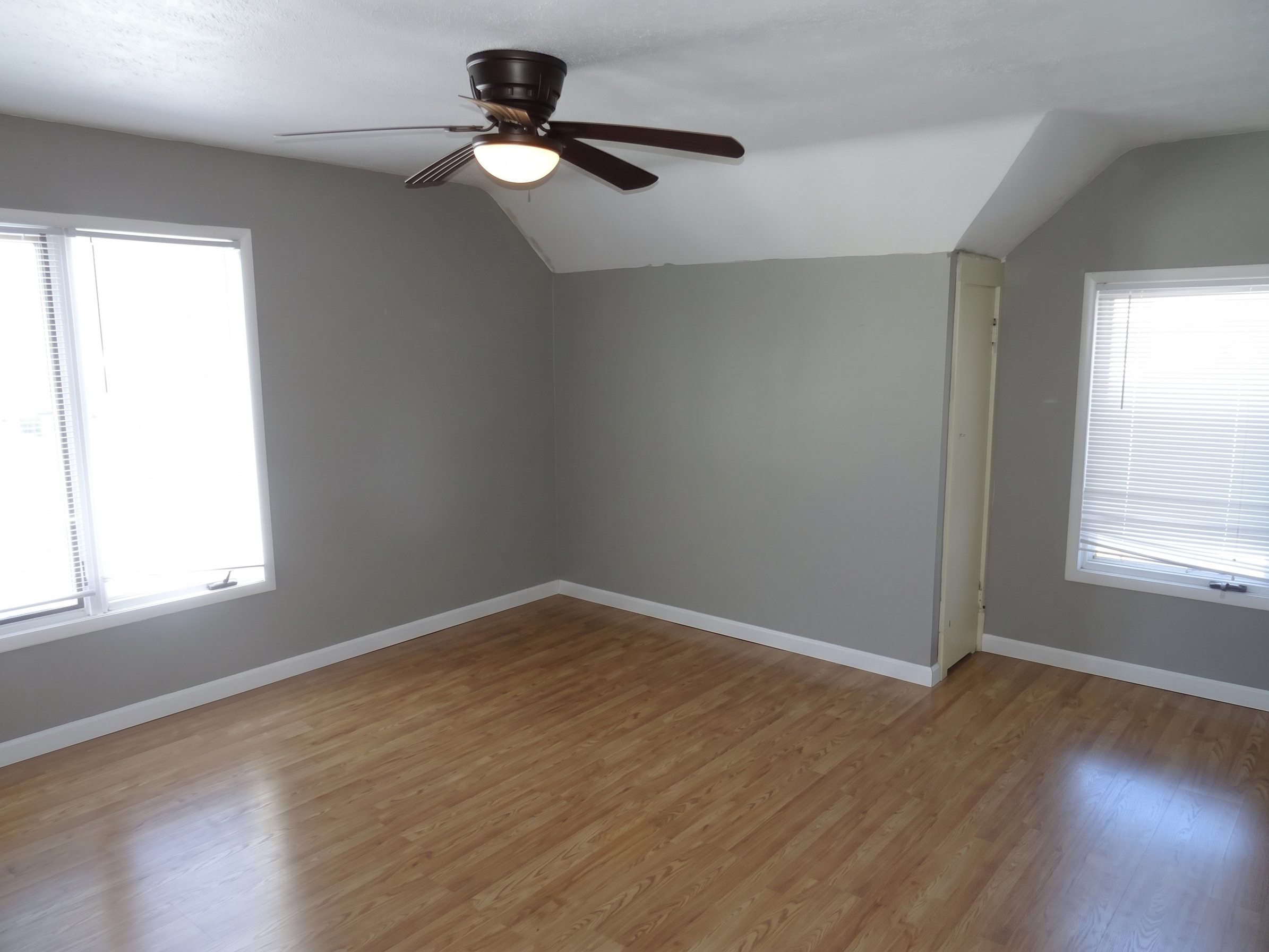Empty upstairs bedroom with gray walls, laminate flooring and a ceiling fan, in a house near Niagara, ND, with the bed digitally removed